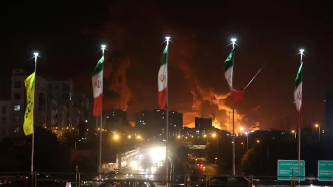 Teheran po izraelskich atakach. Irańskie flagi powiewają na tle pożaru. 