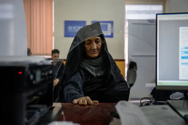 یوه عمر خوړلې مېرمن لیدل کېږي چې د نوملیکنې ماموریت مخې ته ولاړه ده.