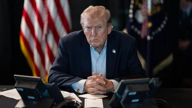 دونالد جی. ترامپ، رئیس‌جمهور ایالات متحده، در تاریخ ۲ مارس ۲۰۲۶ در واشنگتن، پایتخت ایالات متحده، پشت میزی نشسته و در حال نظارت بر عملیات‌های نظامی در جریان عملیات «اپیک فیوری» علیه ایران است؛ در حالی که پرچم‌های آمریکا در پس‌زمینه دیده می‌شوند