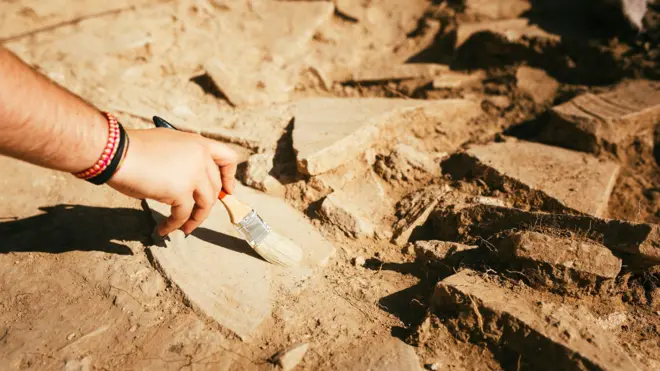Zbliżenie dłoni kobiety używającej pędzla do odkurzania ceramiki na stanowisku archeologicznym