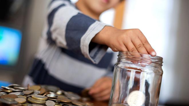 Um menino coloca moedas em uma jarra de vidro