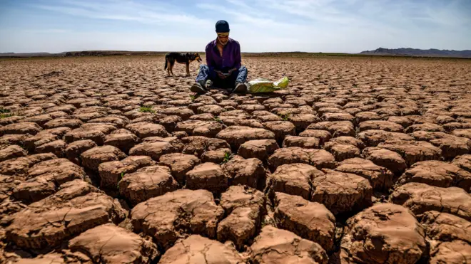 A shepherd checks his mobile phones sitting on cracked earth near Ouled Essi Masseoud in Morocco.