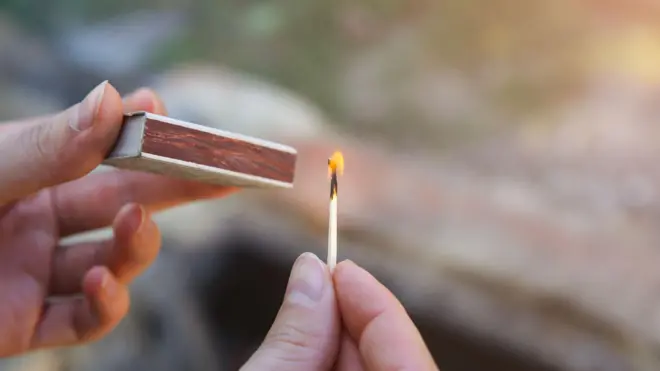 Людина тримає сірники в руках й розпалює вогонь на відкритому повітрі - стокове фото