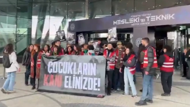 TİP'li öğrenciler Mesleki ve Teknik eğitim zirvesi yazan girişin önünde ellerinde ÇOCUKLARIN KANI ELİNİZDE yazılı bir dövizle slogan atıyor.