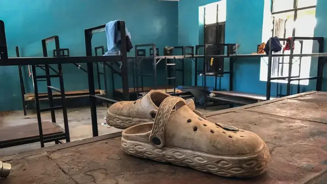 One pair of shoes for inside student dormitory for St Mary's Catholic School for Niger state afta one mass kidnapping. Bunk beds dey visible wit some personal belongings scattered across di room.