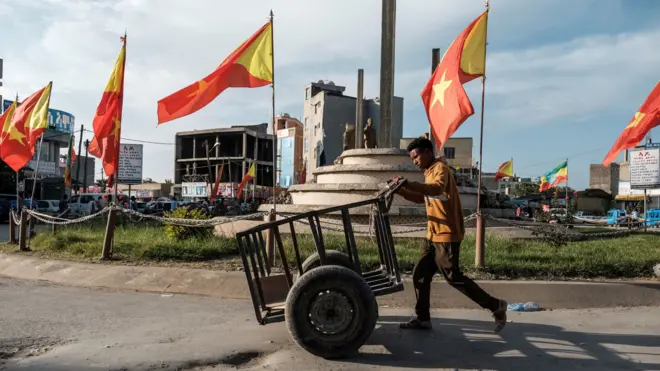 የኢትዮጵያ እና ትግራይ ክልል ባንዲራዎች በተሰቀሉበት አደባባይ ጋሪ እየገፋ የሚያልፍ ወጣት