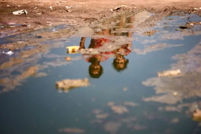 طفلتان فلسطينيتان تجلسان أمام شارع يفيض بمياه الصرف الصحي في دير البلح، غزة