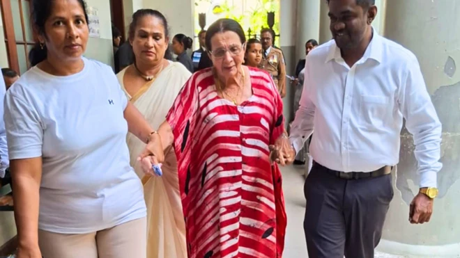 ඩේසි ෆොරස්ට් පුද්ගලයින් දෙදෙනෙකුගේ සහය ඇතිව අධිකරණය වෙත පැමිණෙන අයුරු