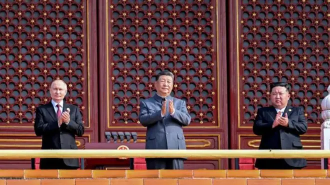 시진핑 중국 국가주석 오른편에 블라디미르 푸틴 러시아 대통령이, 왼편에는 김정은 북한 국무위원장이 서 있다. 2025년 9월 3일 중국 베이징에서 열린 전승절 80주년 기념 군사 퍼레이드에 참석를 박수를 치는 모습 