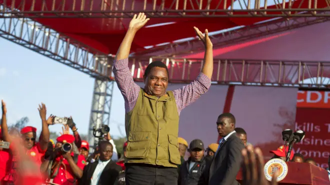 Perezida wa Zambia Hakainde Hichilema yambaye ijaketi y’icyatsi kibisi n’ipantalo y’umukara, azamuye ibiganza asuhuza abayoboke b’ishyaka rye rya UPND.