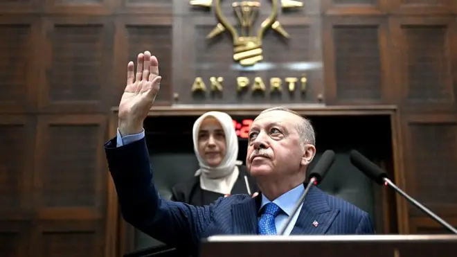 Erdoğan AKP logosu önünde kürsüden elini kaldırmış ve arkasında Özlem Zengin görünüyor