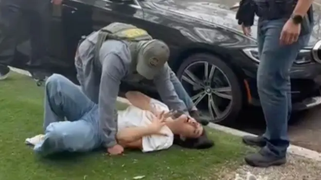 Una mujer en el suelo siendo sujetada por un agente del ICE.