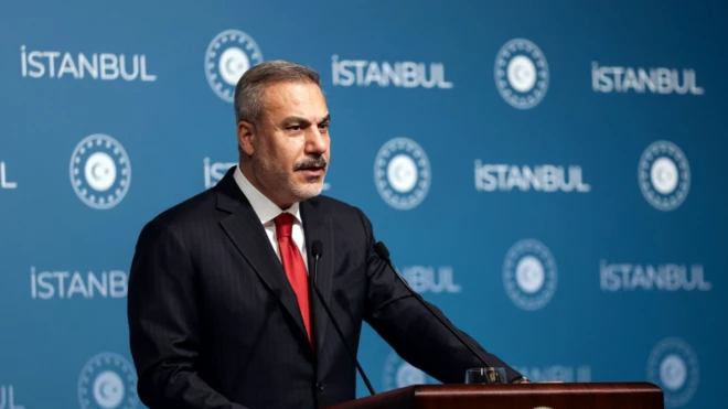 Hakan Fidan yandan görünüyor ve görünmeyen bir yere bakarak konuşuyor. Arkada mavi fonda İstanbul yazıyor.