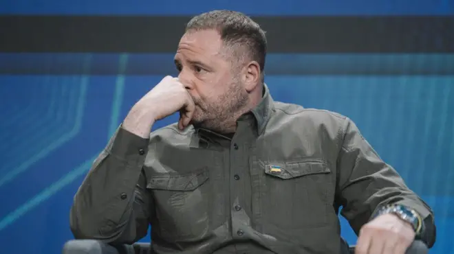 Єрмак в оливковій сорочці сидить у кріслі і сумно дивиться в сторону, тримаючи руку біля обличчя 