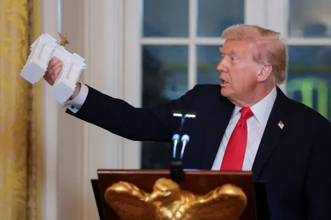 Президент США Дональд Трамп тримає модель Тріумфальної арки зі статуєю Леді Свободи на вершині під час бальної вечері у Східній кімнаті Білого дому у Вашингтоні, жовтень 2025