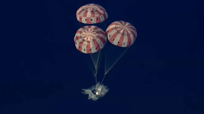La cápsula Orión ameriza asistida por tres paracaídas de colores rojo y blanco.