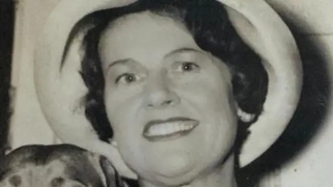 Мюріель Маккей у капелюсі, усміхнена і тримає собаку.