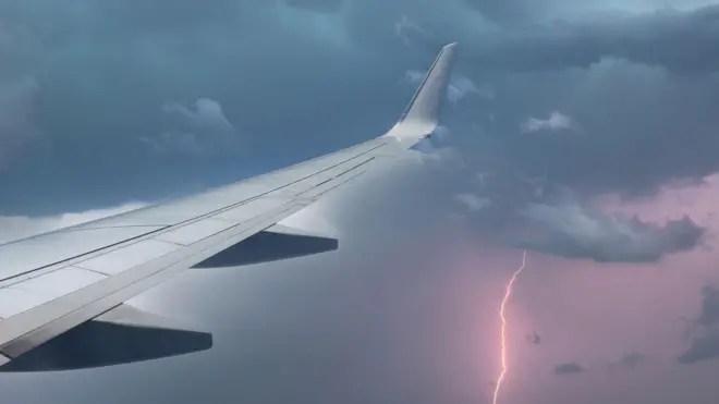 Asa de avião em meio a chuva com raios