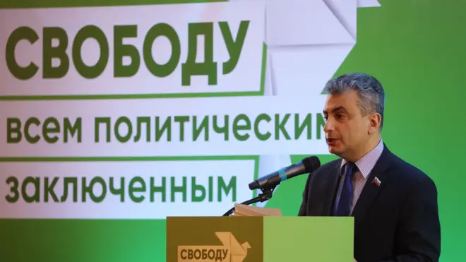 Лев Шлосберг на фоне баннера с надписью «Свободу всем политическим заключенным». 