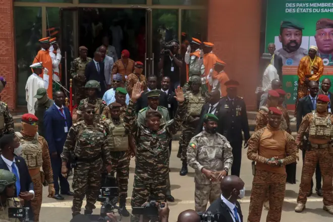Le Général Abdourhamane Tiani du Niger lève les deux mains, à sa droite se trouvent le Colonel Assimi Goita du Mali et le Capitaine Ibrahim Traoré du Burkina Faso. Ils sont tous en tenues militaires devant des appareils photos de journalistes avec d'autres militaires derrière eux.