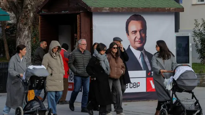 Dve žene guraju kolica, između njih je nekoliko devojaka i dva muškarca, u pozadini bilbord sa slikom Aljbina Kurtija