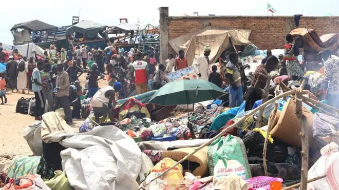 Abantu benshi barimwo abaryamye n'abahagaze n'ibintu vyabo nk'imatera birundnaye, haroboneka uwuryamye ukuboko kwiwe gufashe umutaka usa n'urwatsi rubisi, ku ruhande rw'iburyo haboneka n'akotsi mu Rumonge ku wa 15 Kigarama 2025 