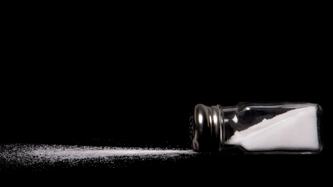 Une bouteille contenant du sel renversée sur une table. Une partie de sel est sur la table avec un fond noir.