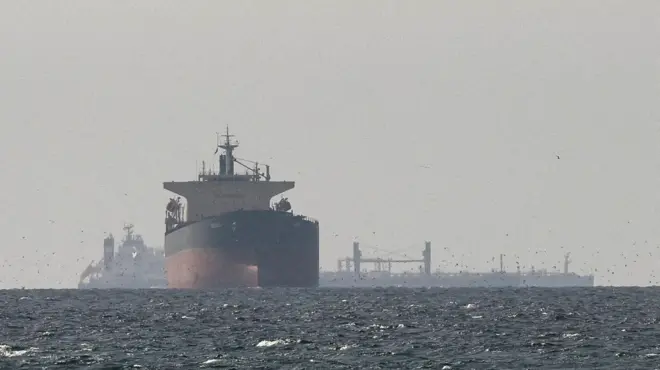 海に大型の貨物船が浮かんでいる。背後には港湾施設の影が見えている。写真は全体的にけぶっている