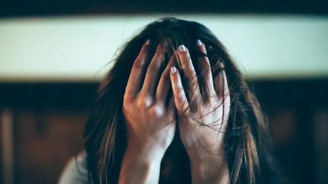 başını iki eliyle tutmuş sıkıntılı bir ifade sergileyen bir kadın