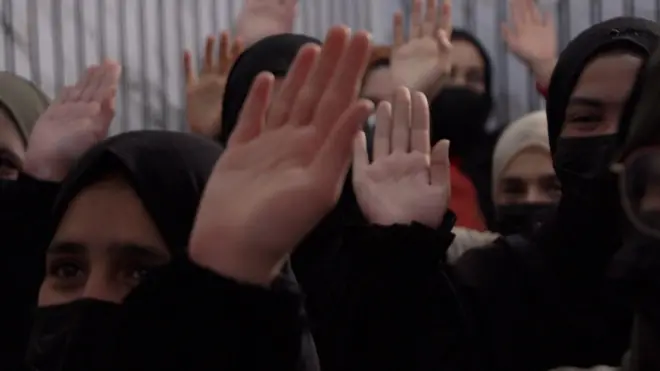 چند دختر با روسری سیاه که دست خود را بلند کرده‌اند. 