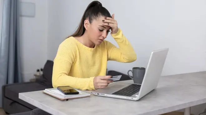 Mulher olhando com preocupação para computador e segurando cartãofluminense e america mg palpitecrédito