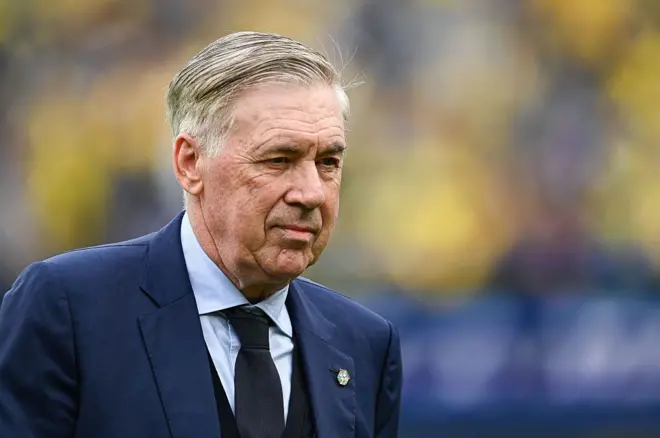 Carlo Ancelotti usando terno e gravata e olhando para um ponto fixo