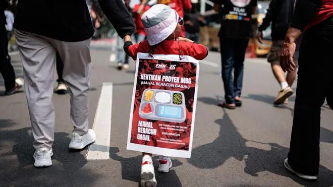 Seorang anak berusia 3 tahun dari anggota Aliansi Gerakan Reforma Agraria (AGRA) membentangkan spanduk di punggungnya yang menentang program makan gratis (MBG) saat demonstrasi pada Hari Tani Nasional di Jakarta pada 24 September 2025.