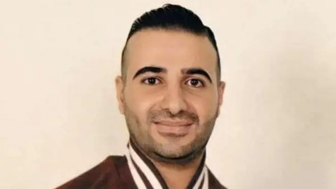 عمّار الحويطات في صورة قديمة مرتدياً قميصاً رياضياً يبدو أنه بني اللون. بشرته حنطية وعيناه وشعره لونهم أسود.