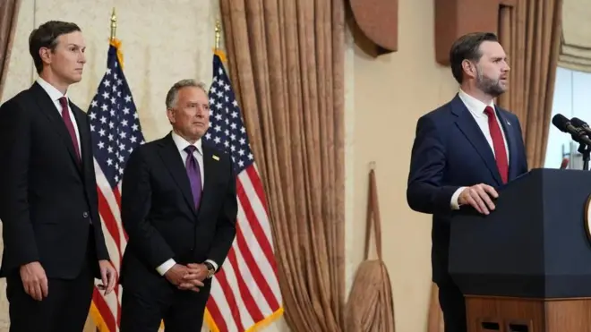 マイクの載った演台に手を添えて話すスーツ姿のヴァンス氏を、後ろからウィトコフ氏とクシュナー氏が見ている。星条旗が並んでいる。