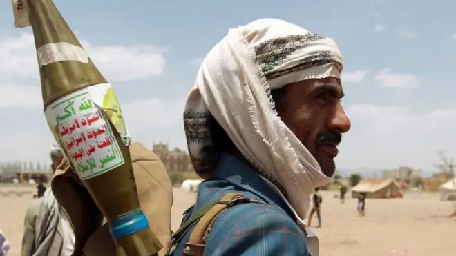 یکی از اعضای حوثی‌ها در حالی که خمپاره‌ای بر دوش دارد و بر روی خمپاره نوشته شده: مرگ بر آمریکا، مرگ بر اسرائیل، الله اکبر