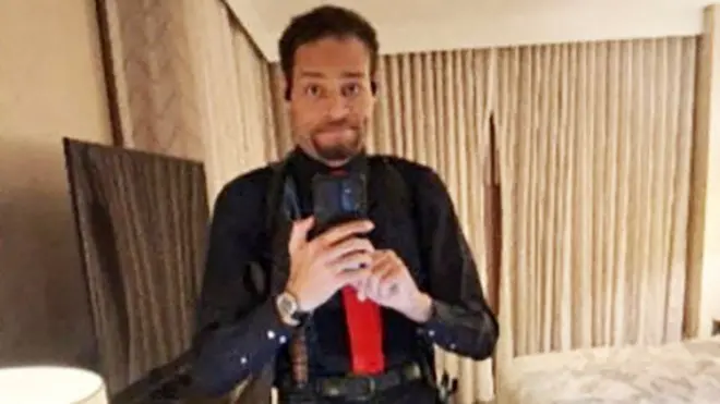 Cole Tomas Allen takes a selfie in a mirror. He is wearing a black shirt and red tie