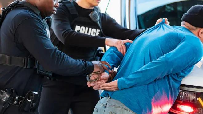 Black woman in black outfit arresting man on blue