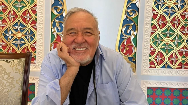 İlber Ortaylı'nın gülerken baktığı bir fotoğrafı. Arkada işlemeli mobilyalar var.