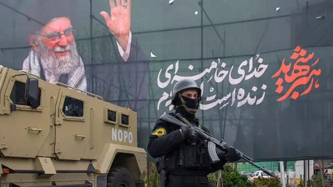 28 Mart 2026'da İran'ın Tahran kentinde, bir polis memuru zırhlı bir aracın ve ölen dini Lider Ali Hamaney'in posterinin yanında duruyor.