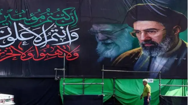 Aworan Oloogbe Ayatollah Ali Khamenei lori patako, wọn kọ keu si ara patako naa, bẹẹ ni ọkunrin kan wa nisalẹ rẹ.