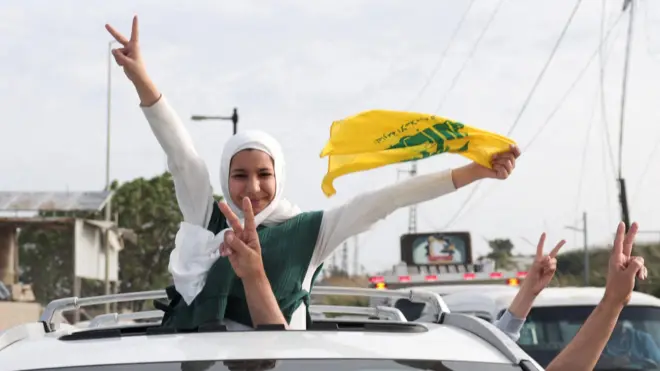 Lübnanlılar ateşkesi kutluyor. Beyaz başörtülü bir kadın arabanın üst camından dışarı çıkmış bir halde ve bir elinde Lübnan bayrağı bir eliyle barış işareti yaparak kameraya bakıyor, araçtan barış işareti yapan başka eller de uzanmış
