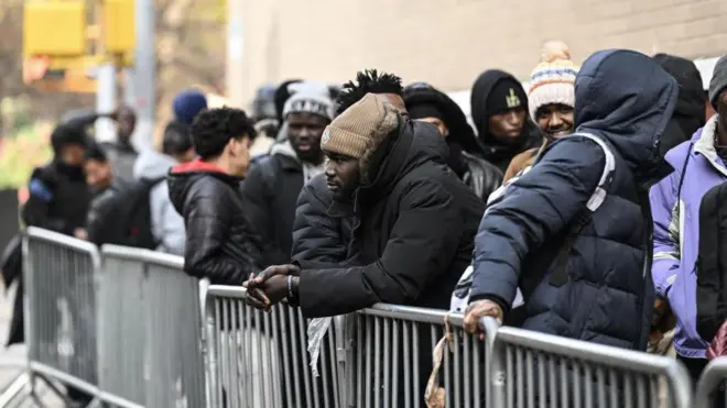 Large number of pipo wey wear black hoodies, one man put hand on di iron barricade wit head warmer.