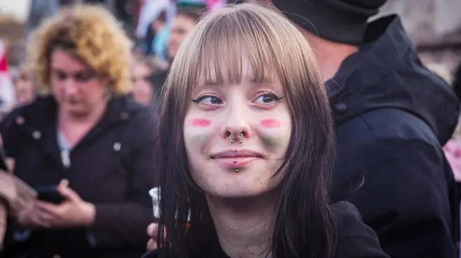 Burnu delik bir genç kız, kahkülleri var. Yanaklarına macar bayrağı renkleri boyalı