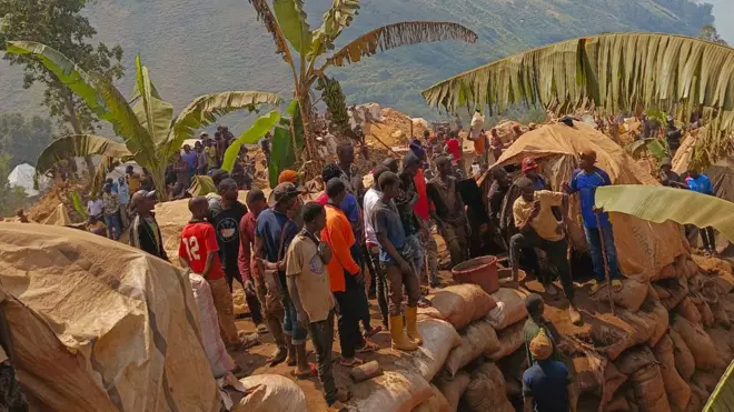 Un groupe de personnes se tient debout en regardant vers le bas dans un puits de mine où un effort de sauvetage est en cours.