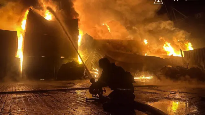 Пожежник присів на землі, він гасить пожежу на контейнерах вночі 