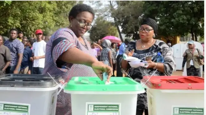 Aworan awọn obinrin meji to n dibo, awọn ike idibo naa wa niwaju wọn, bẹẹ ni awọn oludibo mi-in naa wa nibẹ