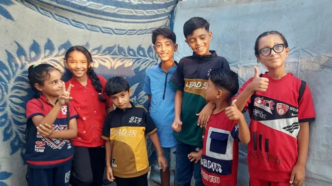 مجموعة من الأطفال الصغيرة تقف مبتسمة داخل خيمة.