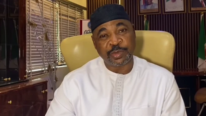 MC Oluomo wọ aṣọ funfun, ó dé fìlà olómi aró, ó ń wo ọ̀ọ́kán