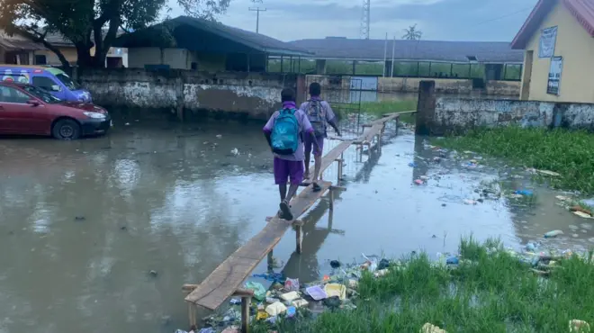 Two school boys dey walk on wooden bridge